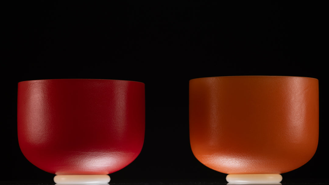 Two frosted crystal singing bowls, one red and one orange, against a black background.