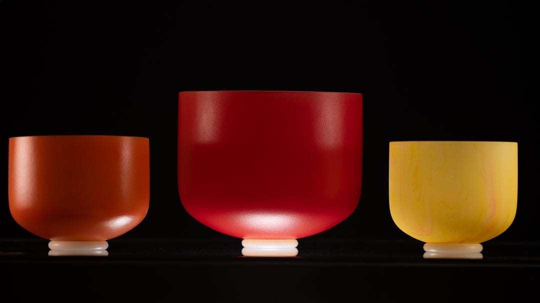 A set of three frosted crystal singing bowls in different sizes, with colors ranging from red to yellow, displayed in a line.