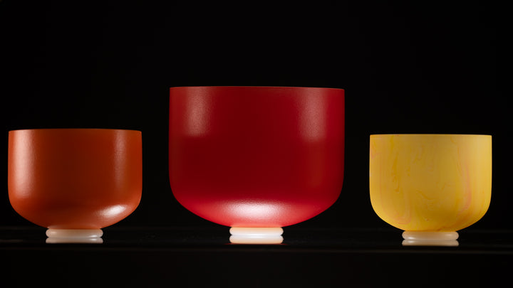 A set of three frosted crystal singing bowls in different sizes, with colors ranging from red to yellow, displayed in a line.