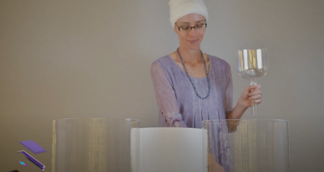 A person is holding a clear quartz crystal singing bowl in their hand, with a white light quartz bowl displayed in the foreground.