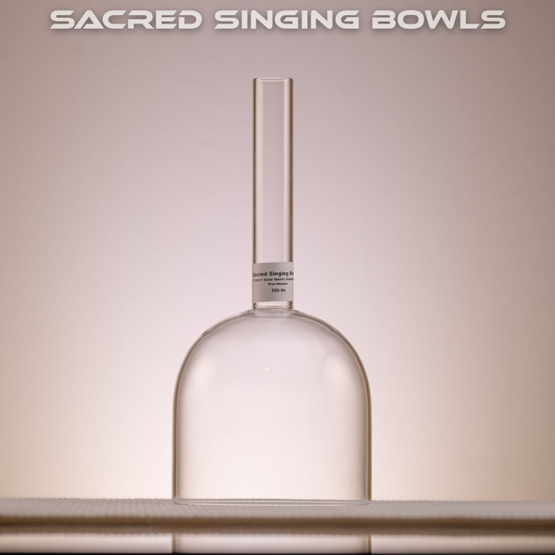 A clear quartz crystal singing bowl with a handheld design, placed on a surface with a label reading 'SACRED SINGING BOWLS'.