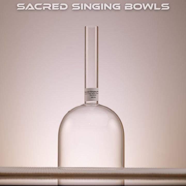 A clear quartz crystal singing bowl with a handheld design, placed on a surface with a label reading 'SACRED SINGING BOWLS'.