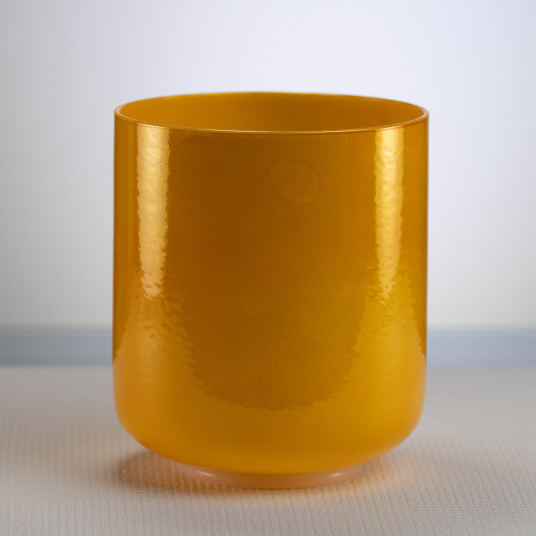 A yellow, honeycomb colored singing bowl placed on a flat surface.