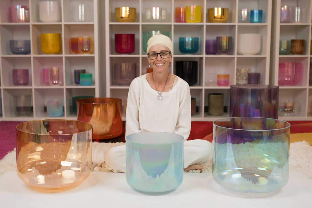 Tara Kaur seated behind three crystal singing bowls arranged in front of a shelf full of crystal singing bowls.