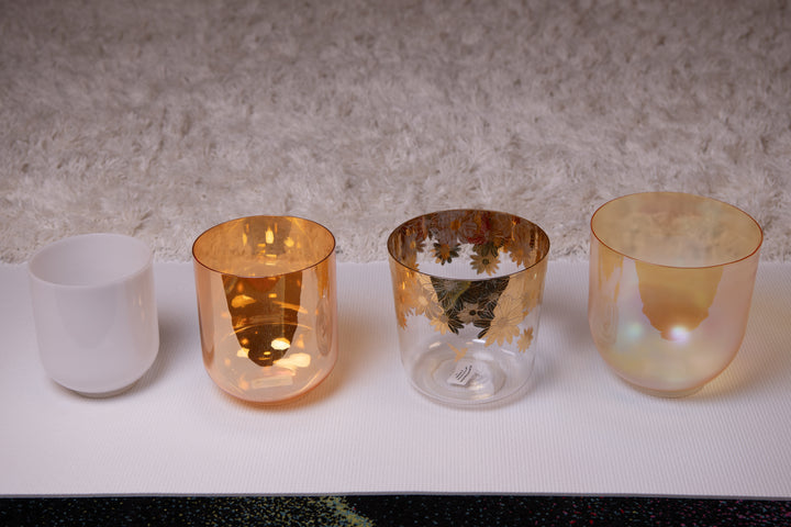 A set of four Sacred Singing Bowl crystal singing bowls in different sizes, placed side by side on a light-colored surface.