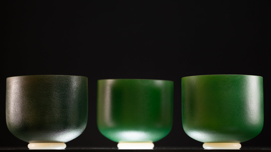 Three frosted green crystal singing bowls with gold inside, displayed side by side against a black background.
