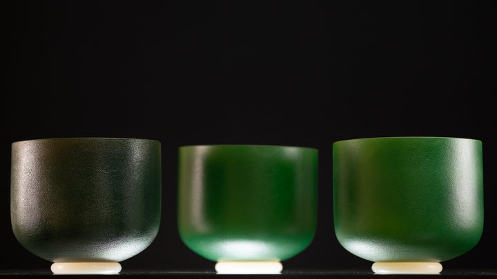 Three frosted green crystal singing bowls with gold inside, displayed side by side against a black background.