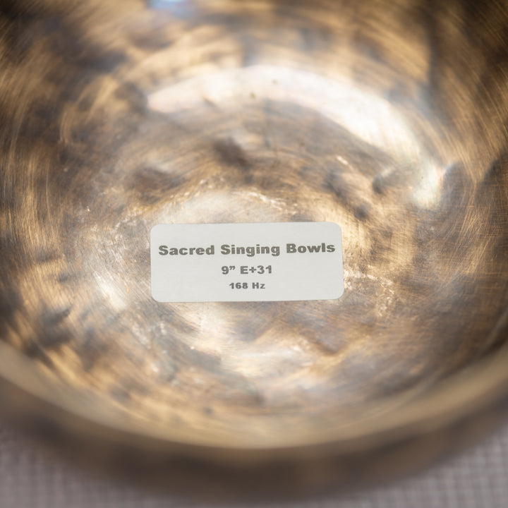 Close-up of a bronze singing bowl with a label indicating 'Sacred Singing Bowls' and specifications.