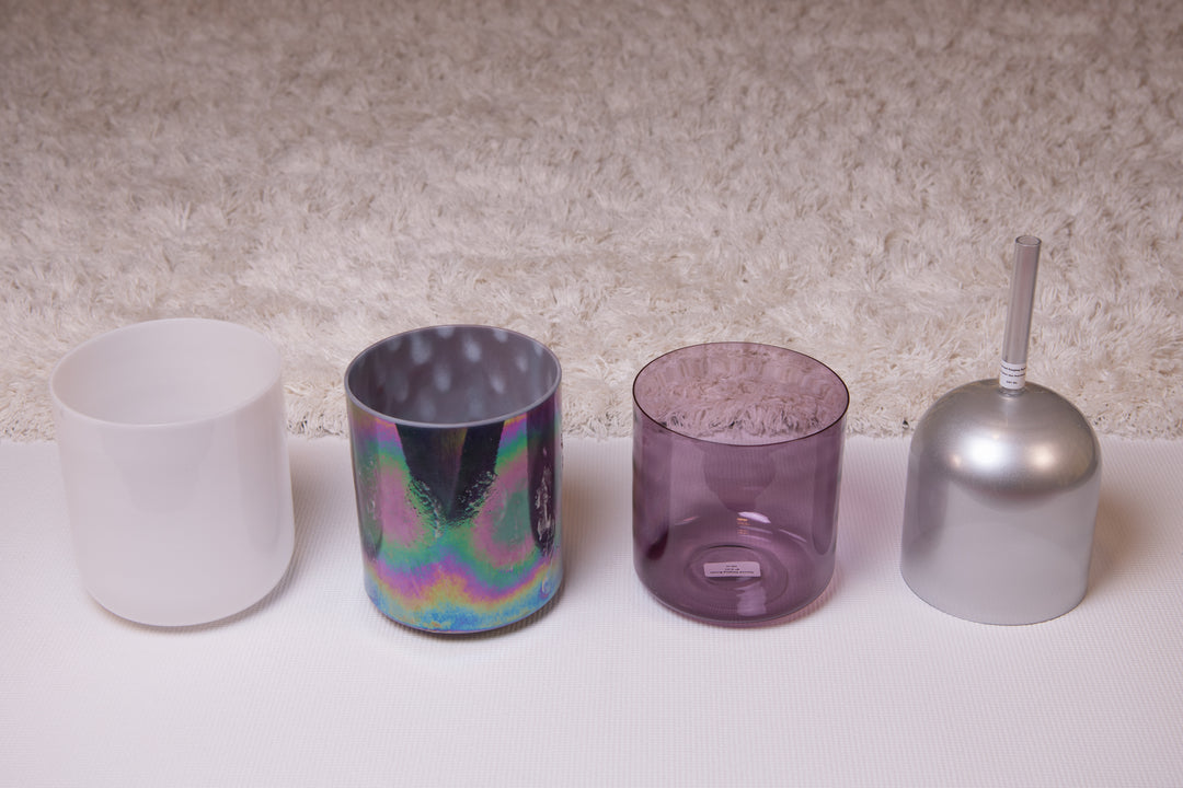 A set of four crystal singing bowls in different sizes with a white mallet, displayed on a textured background.