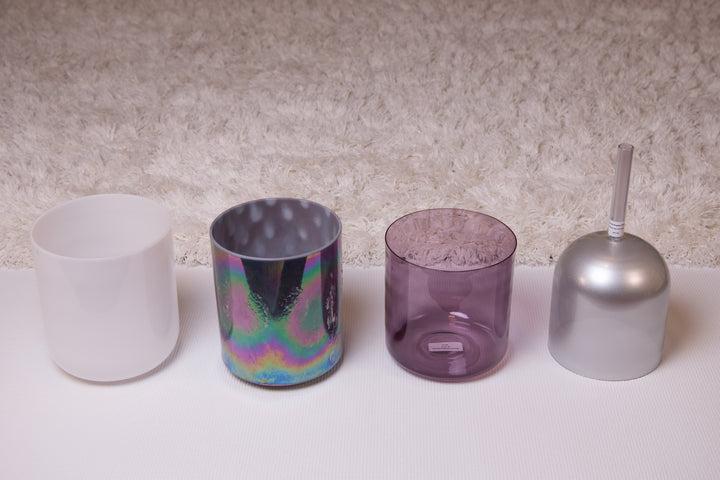 A set of four crystal singing bowls in different sizes with a white mallet, displayed on a textured background.