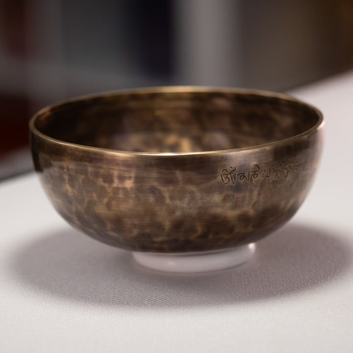 Bronze singing bowl with engraved text on a white surface
