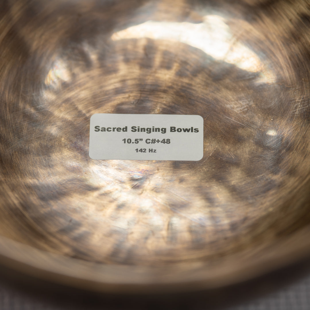 Close-up of a metallic singing bowl with a label indicating 'Sacred Singing Bowls' and dimensions.