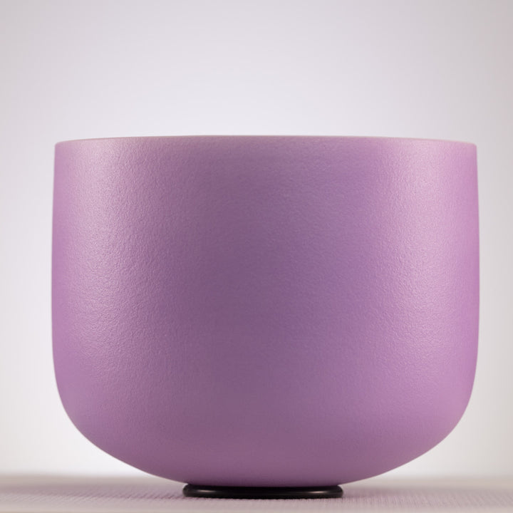 A matte lavender purple ceramic singing bowl with a textured finish, sitting on a small black base against a neutral light gray background.