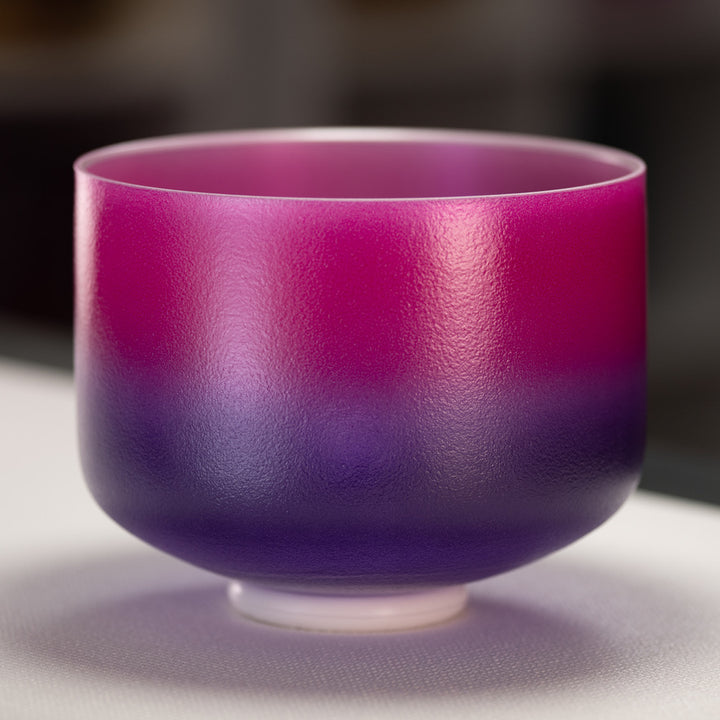 A 10" E-28 Blossoming Heart Frosted Crystal Singing Bowl with a gradient of pink to purple color, silver inside, placed on a white surface.