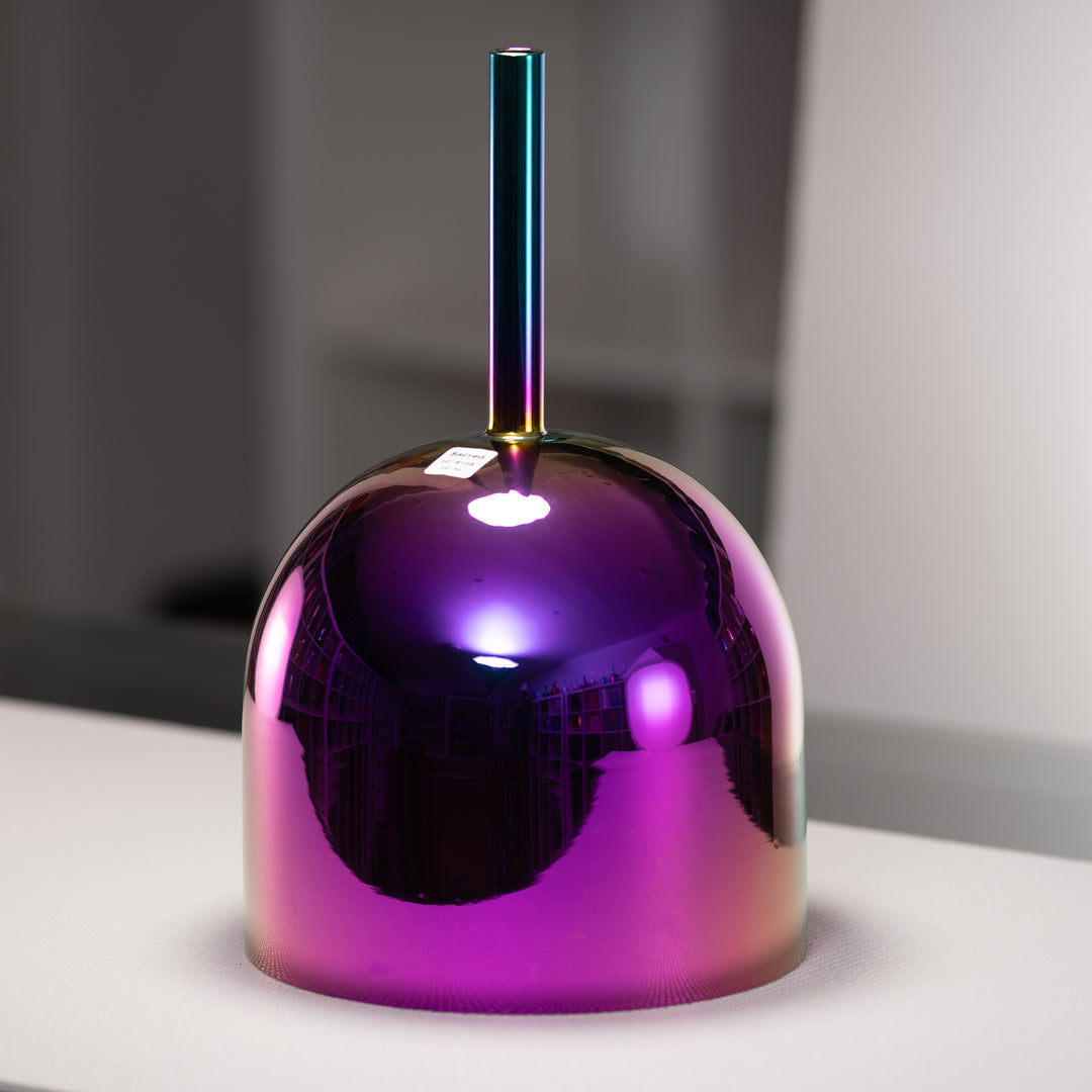 Shiny metallic singing bowl with a gradient color on a reflective surface