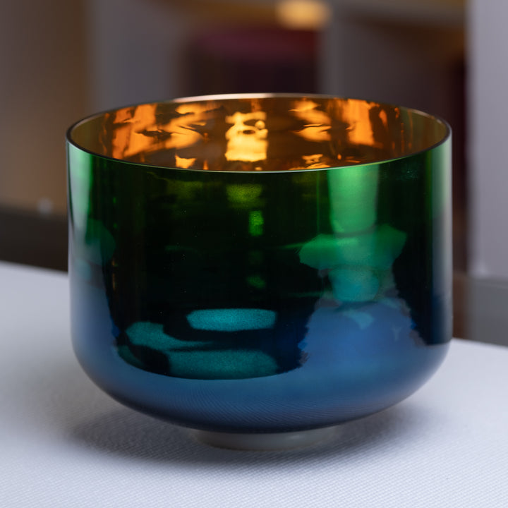 An 11 inch A+4 Divine Earth Crystal Singing Bowl with gold inside, featuring a dark blue and gold color scheme, placed on a surface with a blurred background.