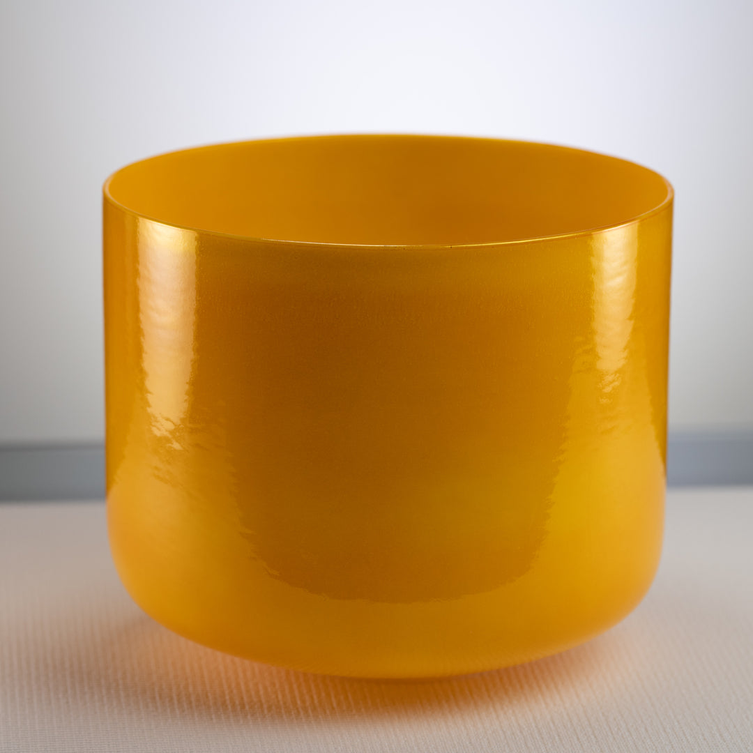 A polished yellow crystal singing bowl with a smooth surface, placed on a flat surface.