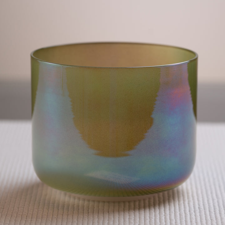 A multicolored crystal singing bowl with a reflective surface, placed on a textured surface.