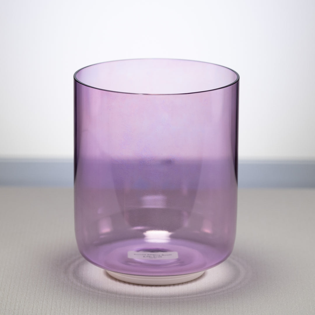 A light purple, 6.75 inch E+26 Lilac Blossom Crystal Singing Bowl placed on a white surface, with a reflective base.