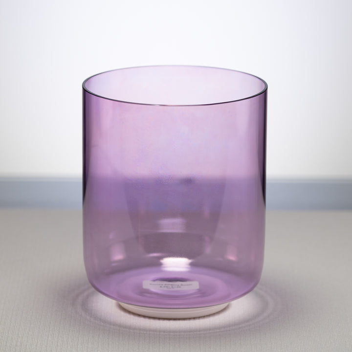 A light purple, 6.75 inch E+26 Lilac Blossom Crystal Singing Bowl placed on a white surface, with a reflective base.
