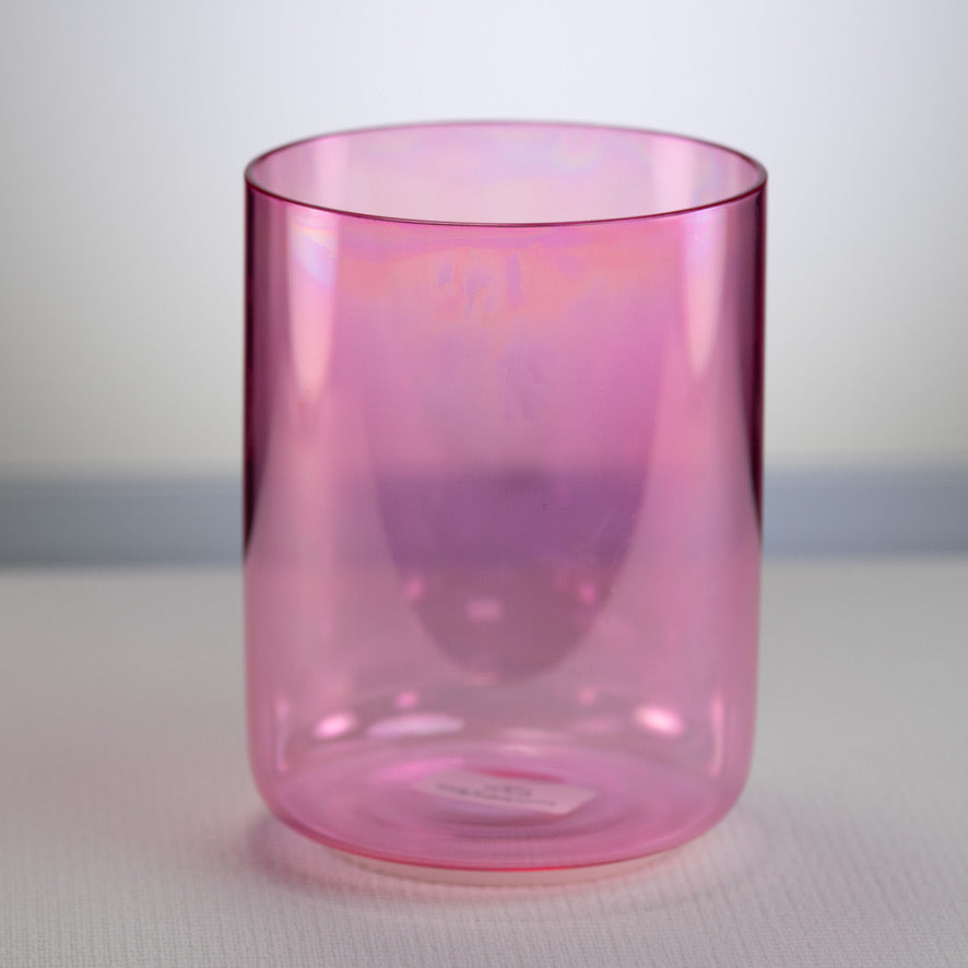 A pink colored crystal singing bowl with a smooth, cylindrical shape, placed on a flat surface.