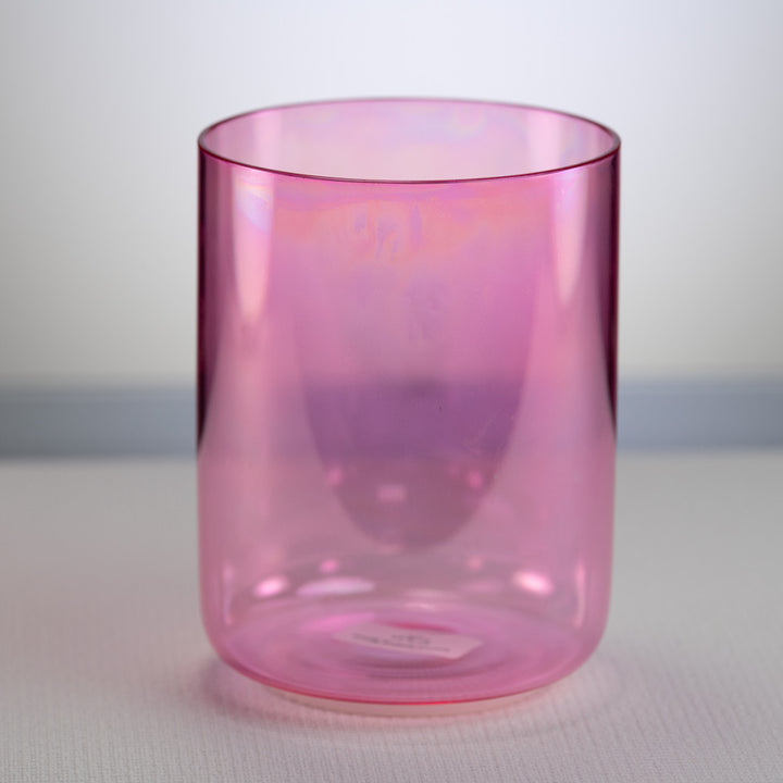 A pink colored crystal singing bowl with a smooth, cylindrical shape, placed on a flat surface.