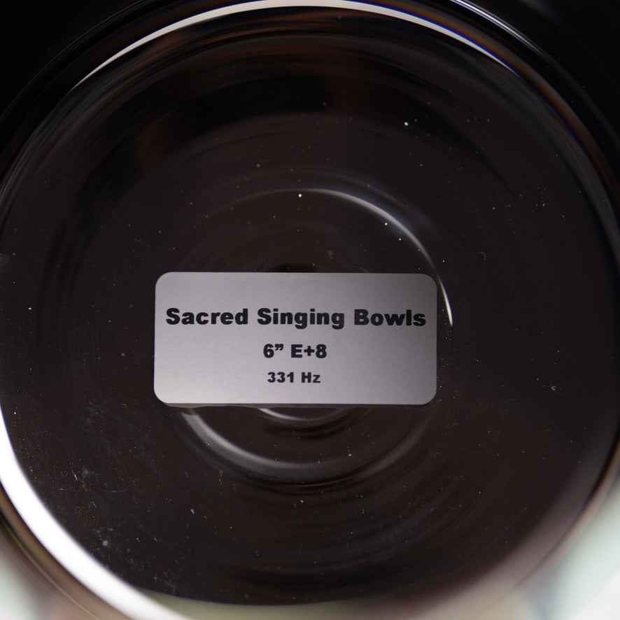 Close-up of a black singing bowl with a label indicating 'Sacred Singing Bowls' and specifications.
