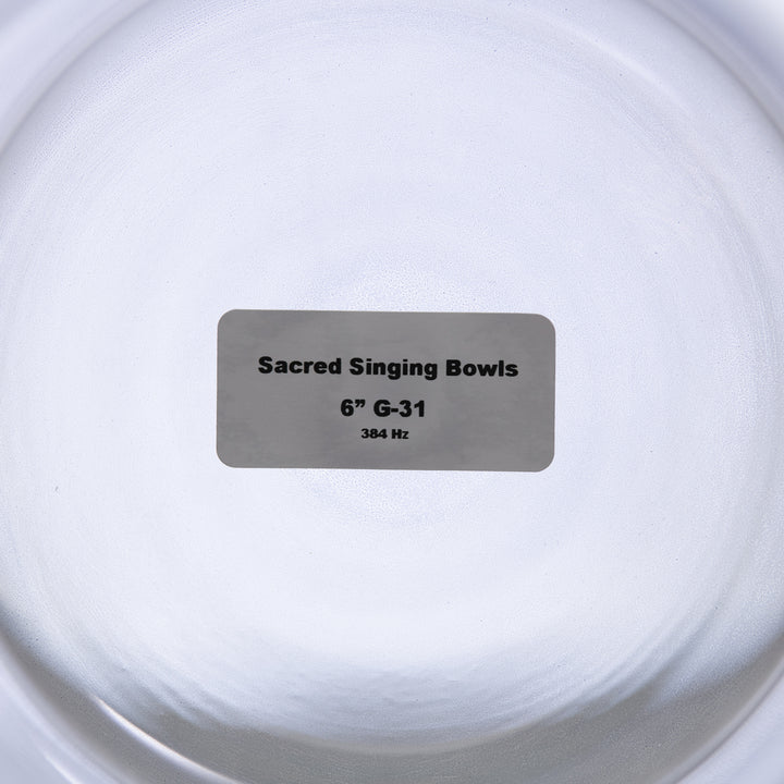 A label placed inside a clear glass singing bowl with the text 'Sacred Singing Bowls 6" G-31 384 Hz'.