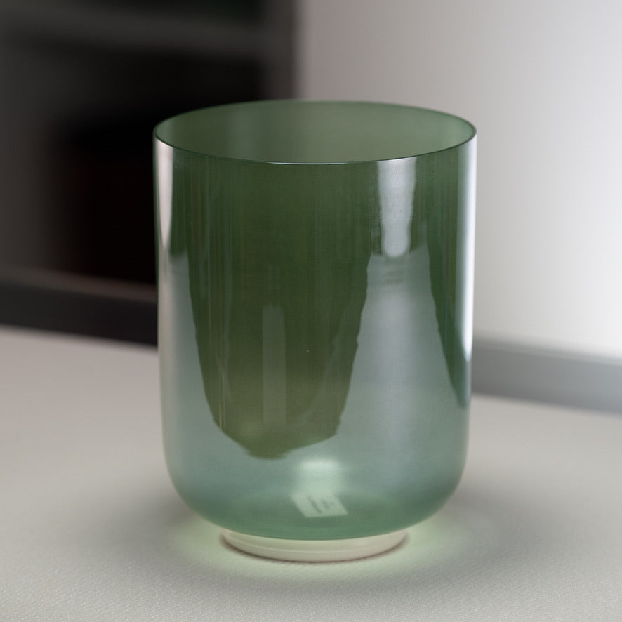 A green quartz crystal singing bowl with a reflective surface, placed on a white surface with a blurred background.
