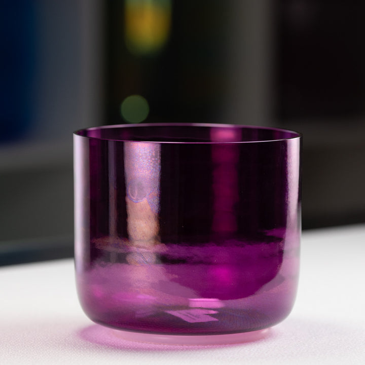A purple quartz crystal singing bowl on a white surface with a blurred background.