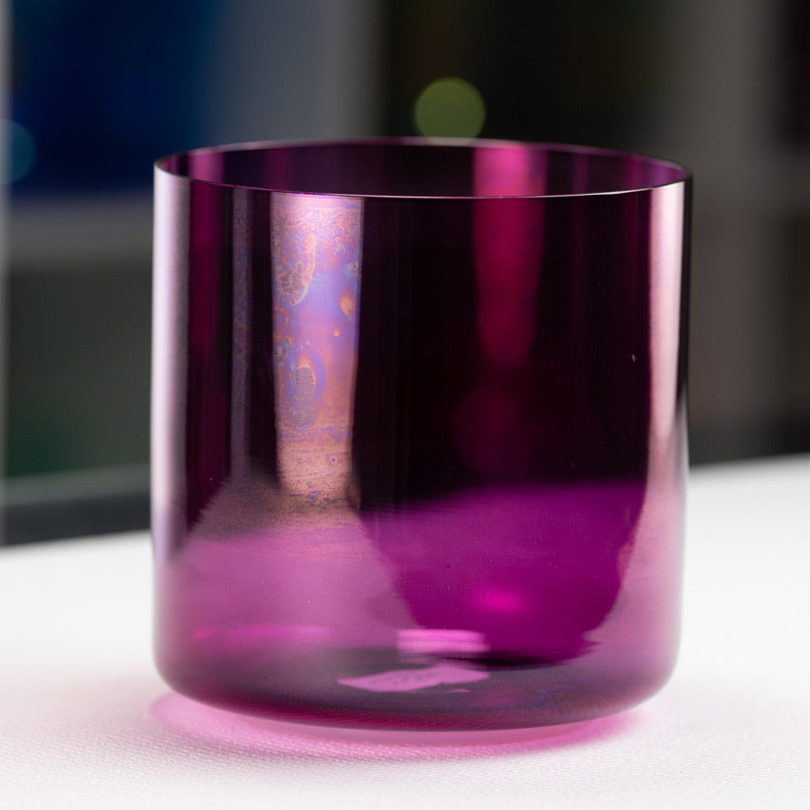 A purple crystal singing bowl with a smooth surface on a white surface with a blurred background.