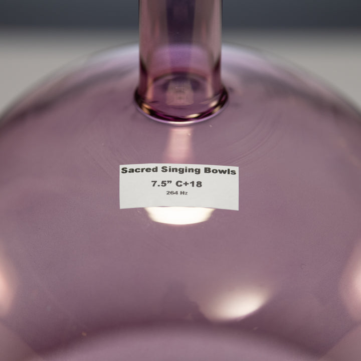 A close-up image of a 7.5" C+18 Solar Violet Handheld Crystal Singing Bowl with a label that reads 'Sacred Singing Bowls".