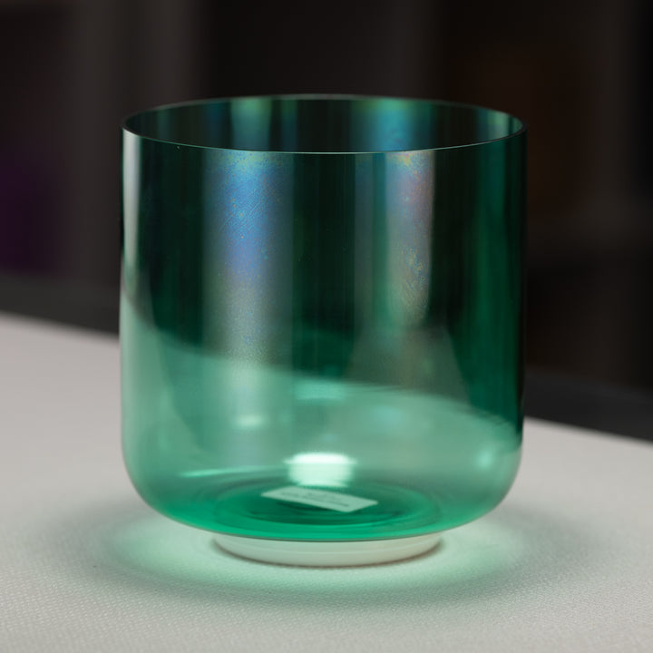 A green quartz crystal singing bowl with a reflective surface, displayed on a white surface with a dark background.