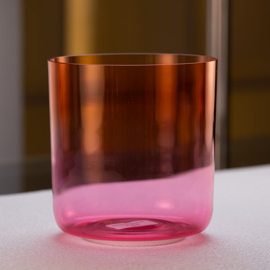 A gradient orange to pink quartz crystal singing bowl placed on a surface.