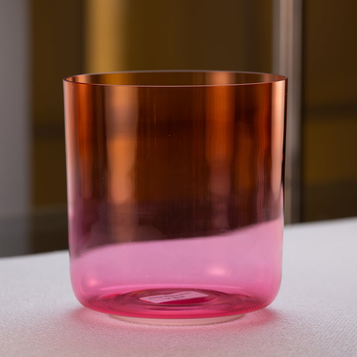 A gradient orange to pink quartz crystal singing bowl placed on a surface.