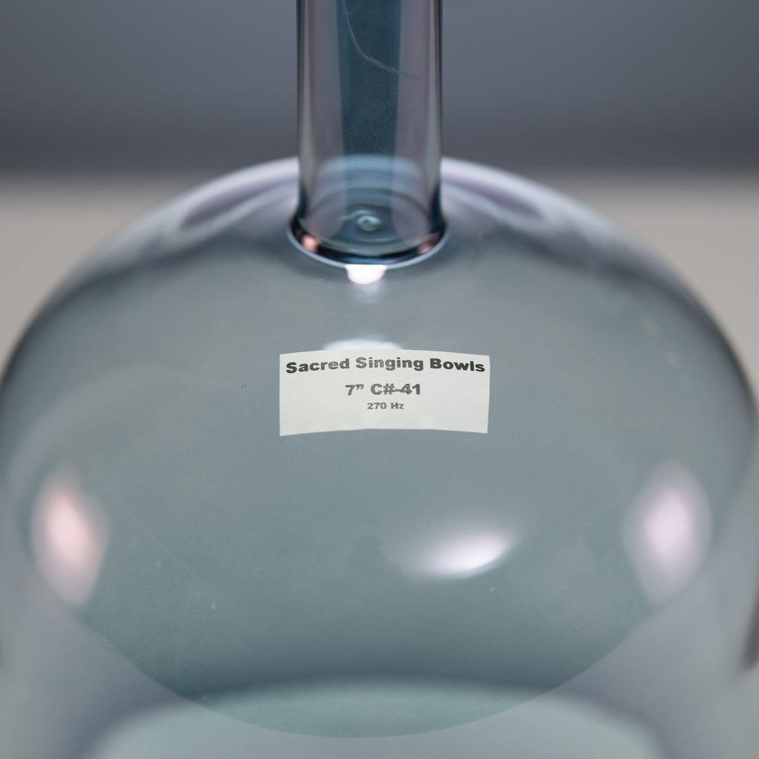 A close-up image of a handheld crystal singing bowl with a label that reads 'Sacred Singing Bowls 7" C#-41.'