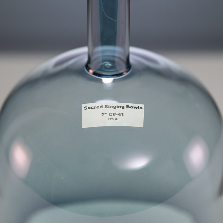 A close-up image of a handheld crystal singing bowl with a label that reads 'Sacred Singing Bowls 7" C#-41.'