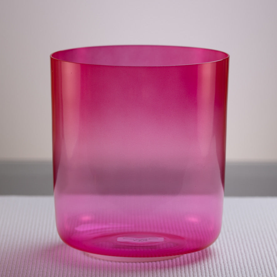 A bright pink, 8-inch D-16 Dreamy Peony Crystal Singing Bowl placed on a textured surface.
