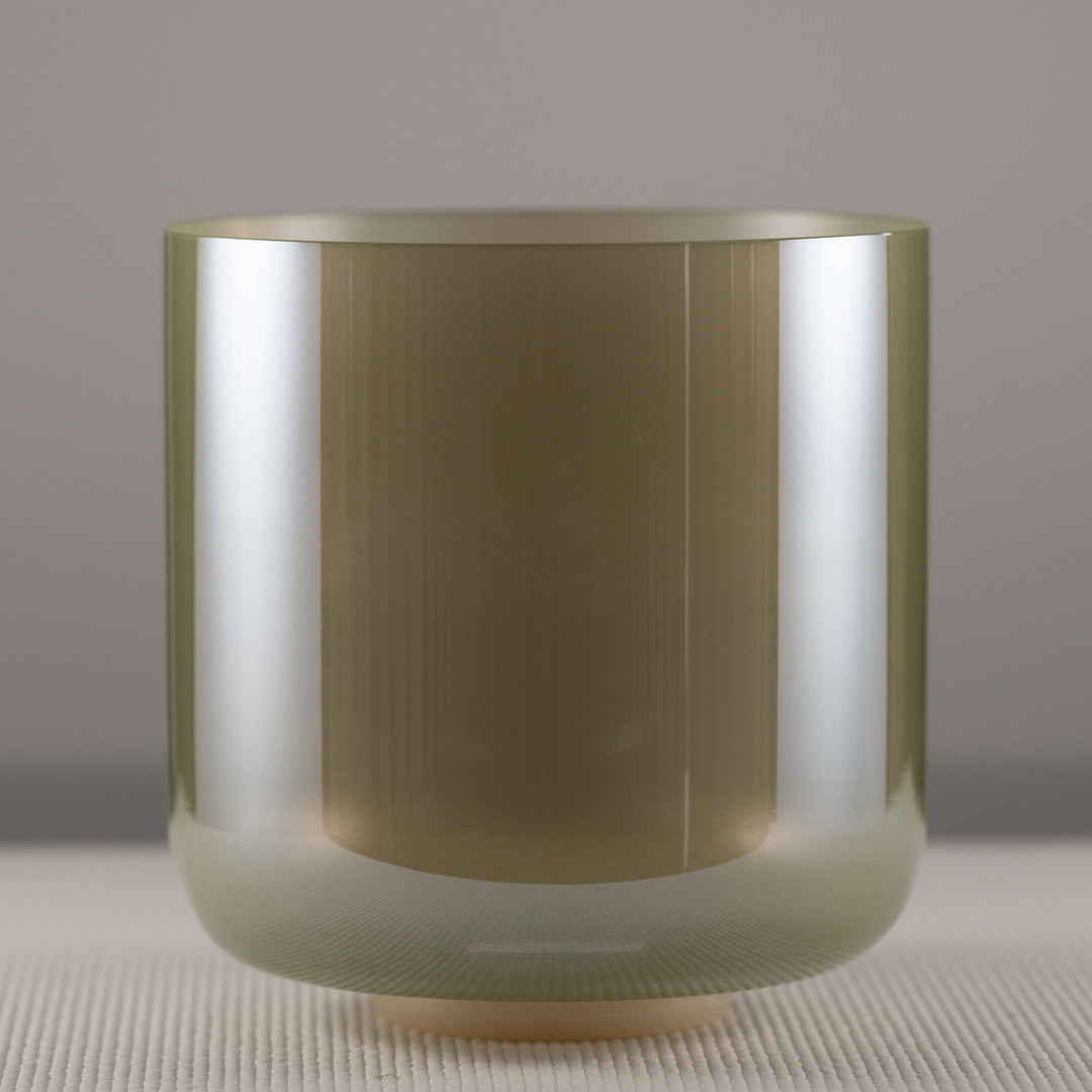 A 9.25 inch quartz crystal singing bowl with a sage green color, placed on a textured surface.
