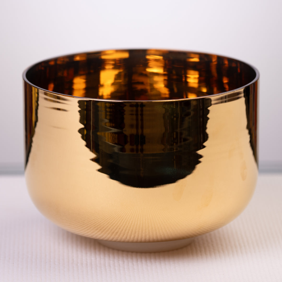 A 9.5 inch B-35 24k gold crystal singing bowl with a bright golden finish, placed on a white surface.