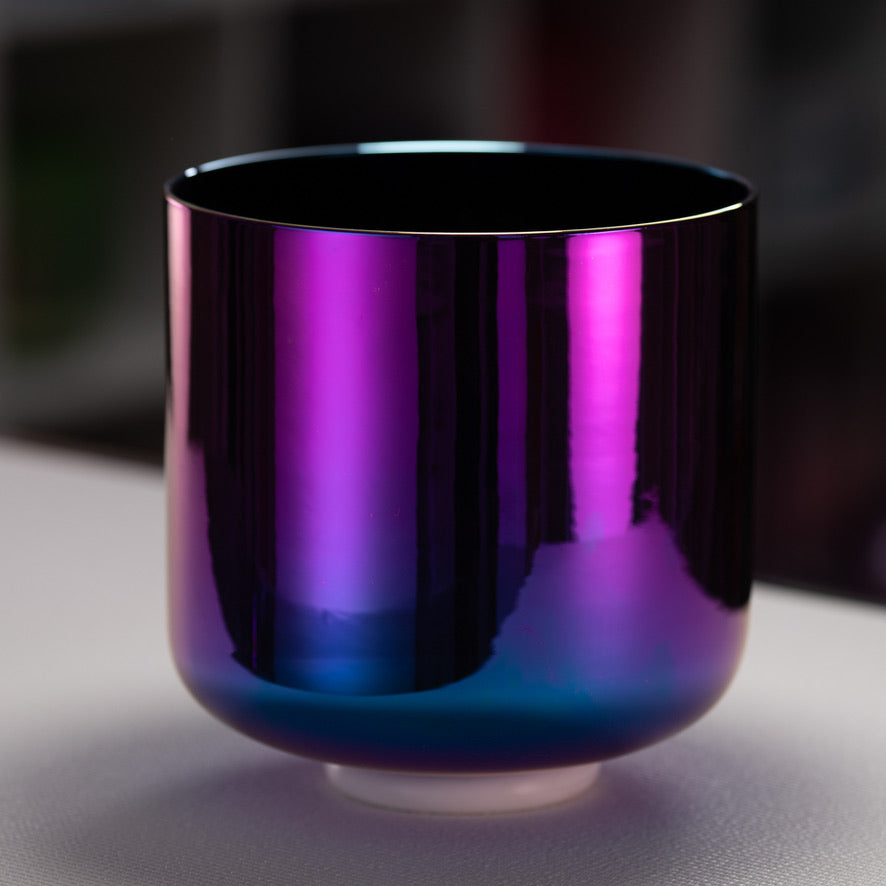 Shiny purple and blue crystal singing bowl on a reflective surface with a blurred background