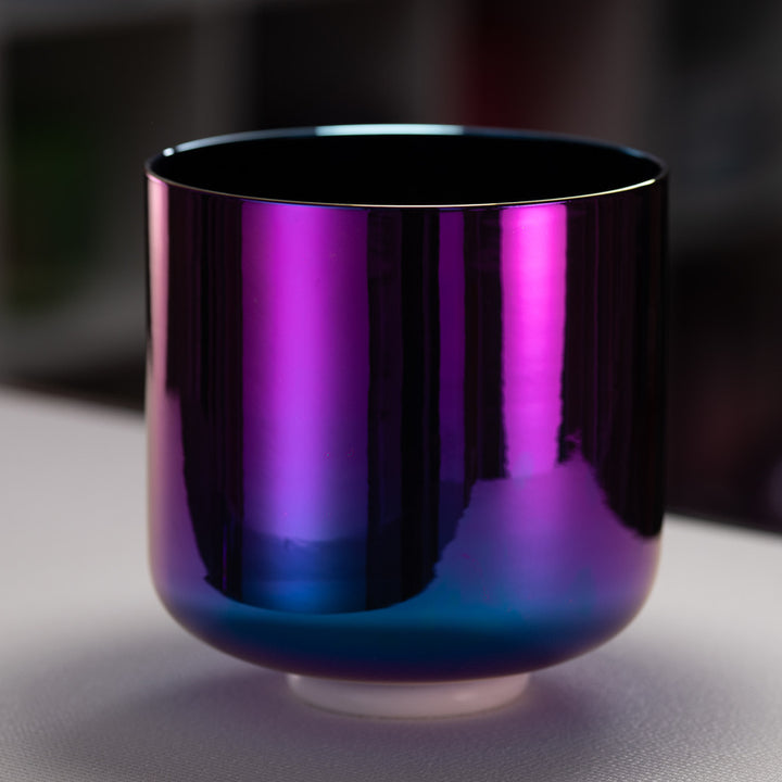 Shiny purple and blue crystal singing bowl on a reflective surface with a blurred background
