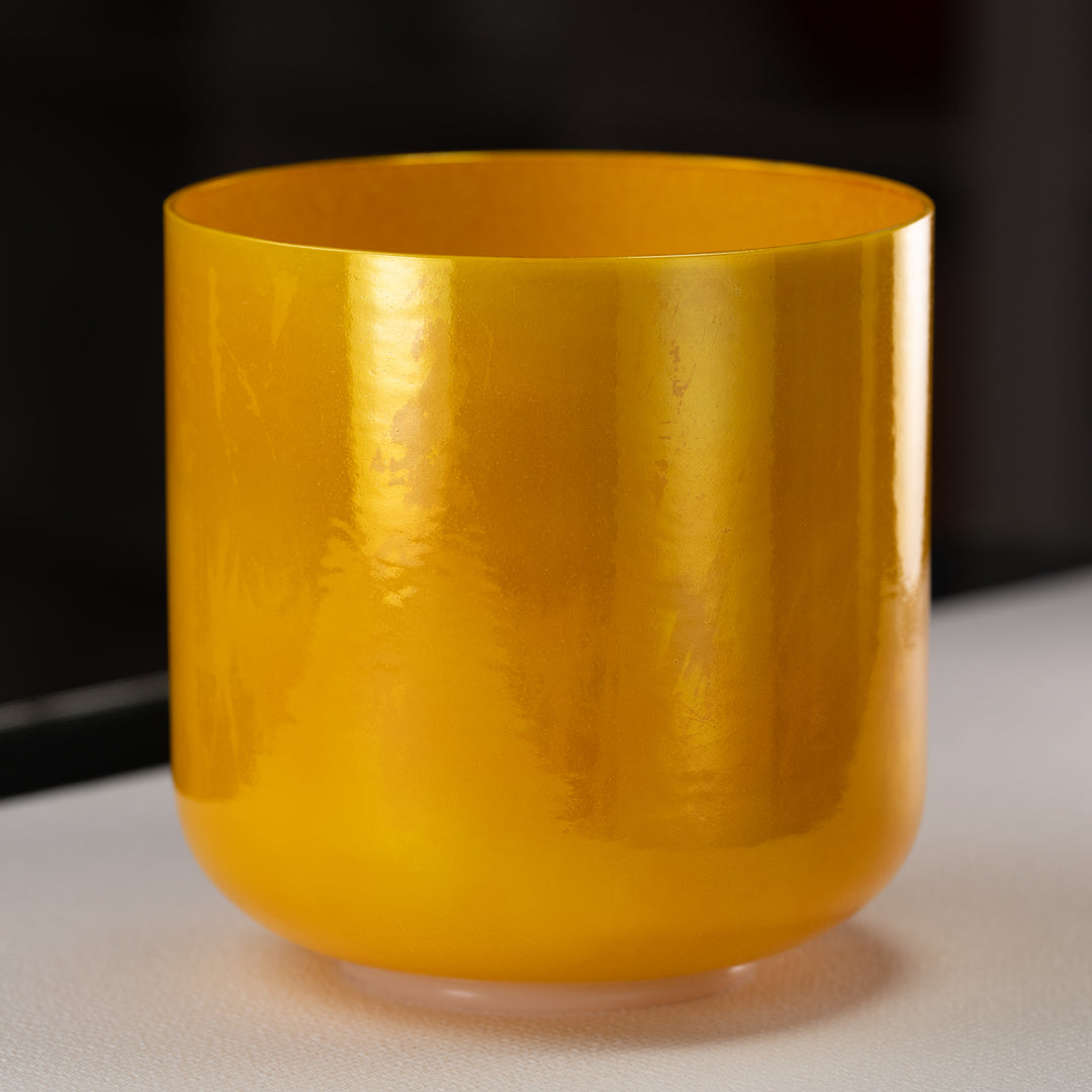 A polished golden yellow quartz crystal singing bowl with a smooth surface, placed on a dark background.