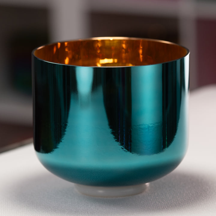 Teal and gold metallic singing bowl on a reflective surface with blurred background
