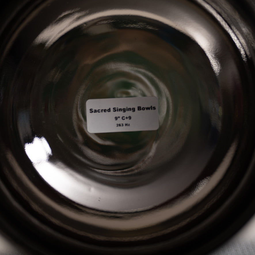 Close-up of a black singing bowl with a label indicating 'Sacred Singing Bowls' and specifications.