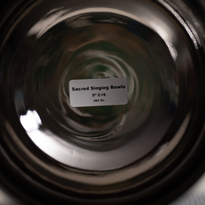 Close-up of a black singing bowl with a label indicating 'Sacred Singing Bowls' and specifications.