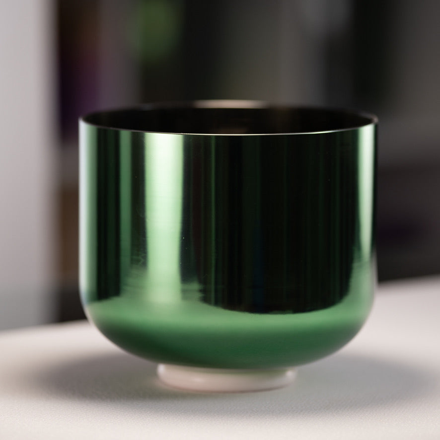 Green metallic bowl on a reflective surface with a blurred background