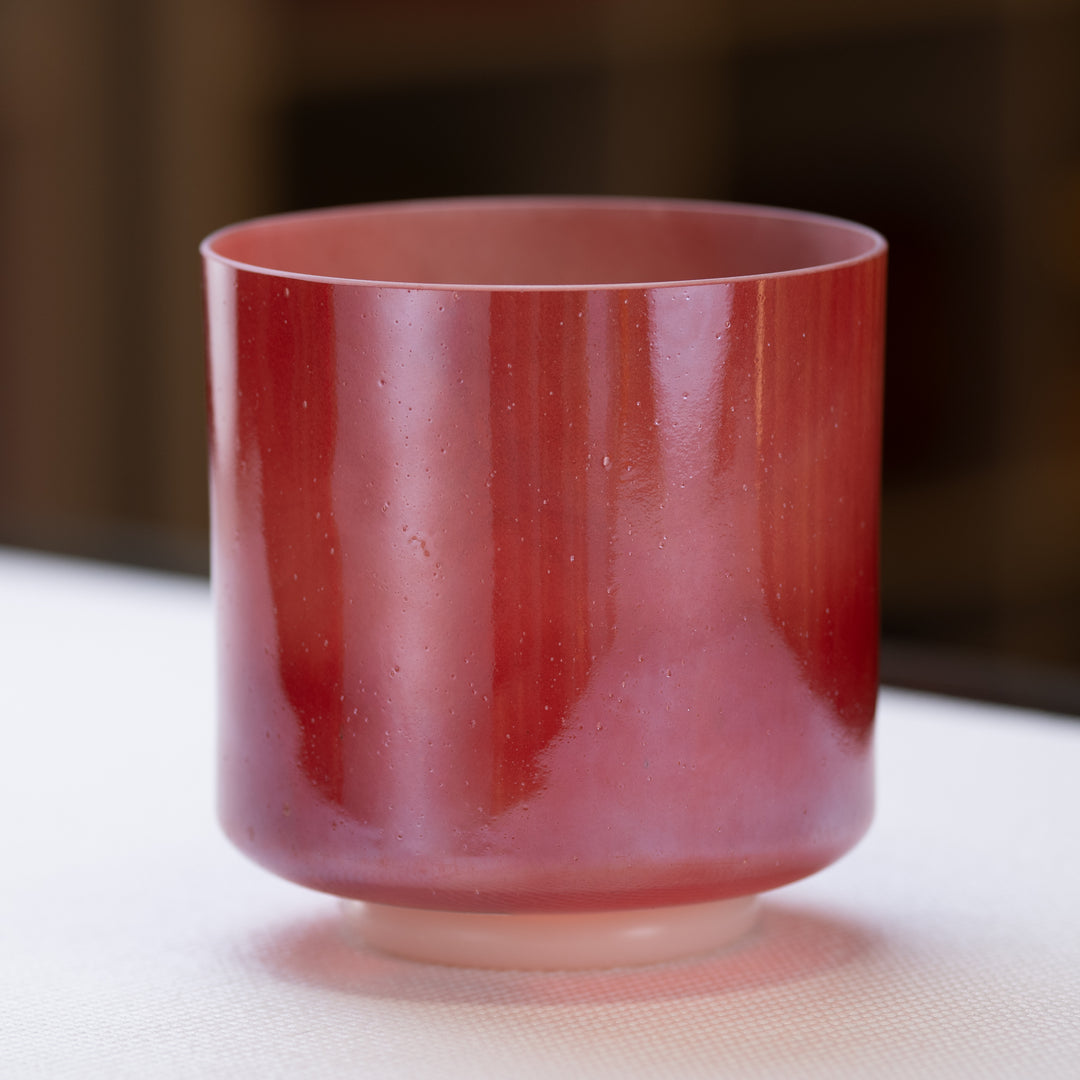 A 7-inch crystal singing bowl with a ruby red exterior and white light aura gold interior, placed on a light surface.