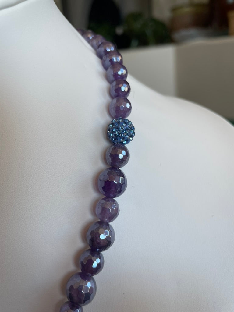 Purple beaded necklace on a mannequin with a blurred background