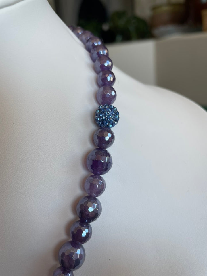 Purple beaded necklace on a mannequin with a blurred background